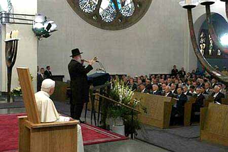 Benedict XVI seated at a synagogue while a rabbi speaks